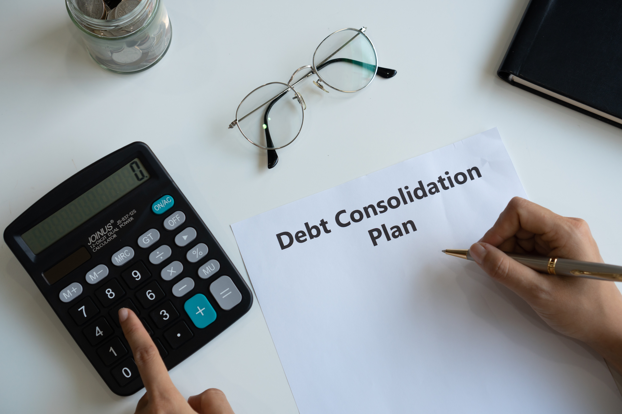 Woman writing debt consolidation plan in paper while using calculator on desk. Copy space, top view.